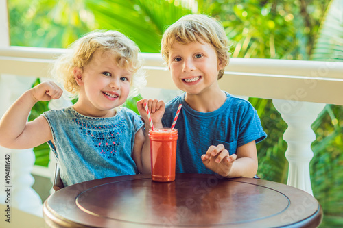 Children boy and girl drink orange smoothie from papaya photo