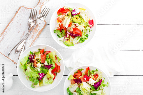 Healthy vegetable salad with fresh greens, lettuce, avocado, tomato, seet pepper and  goat cheese. Delicious and nutritious diet dish for breakfast. Salad bowls on white wooden background