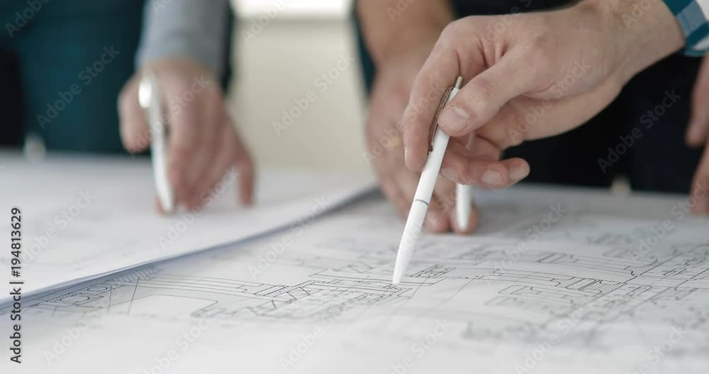 Close-up of the hand of three office workers on a table with blueprints Close-up of the hand of three office workers on a table with blueprints