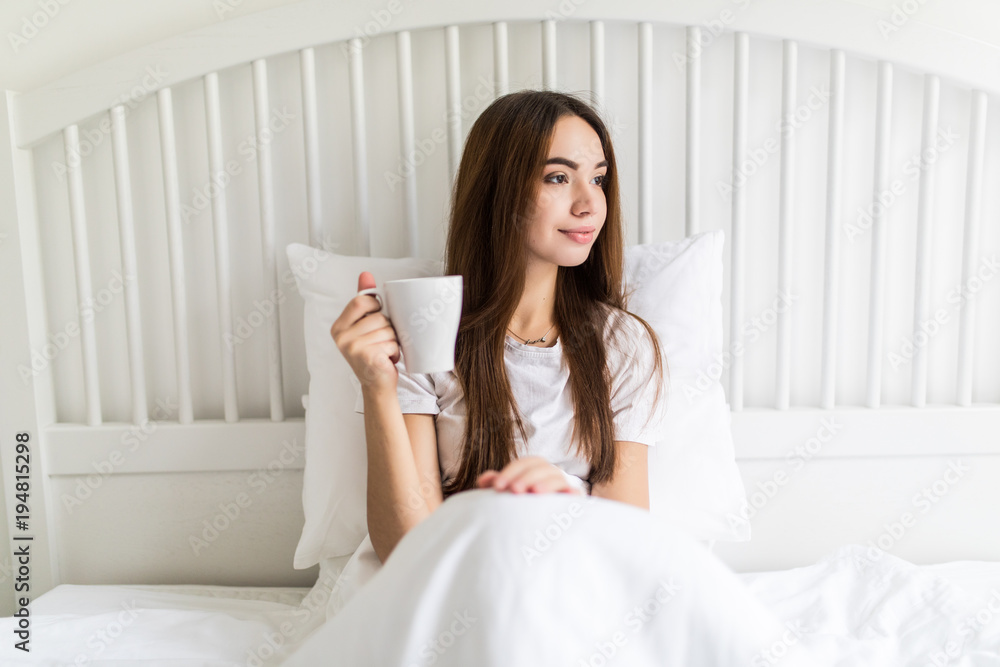Happy young woman with cup of coffee or tea in bed at home bedroom Happy young woman with cup of coffee or tea in bed at home bedroom