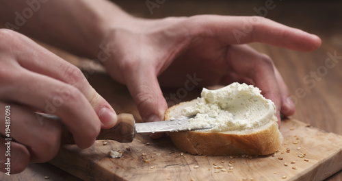 Schilderij op canvas man hands spreading cream cheese on baguette slice on wood board