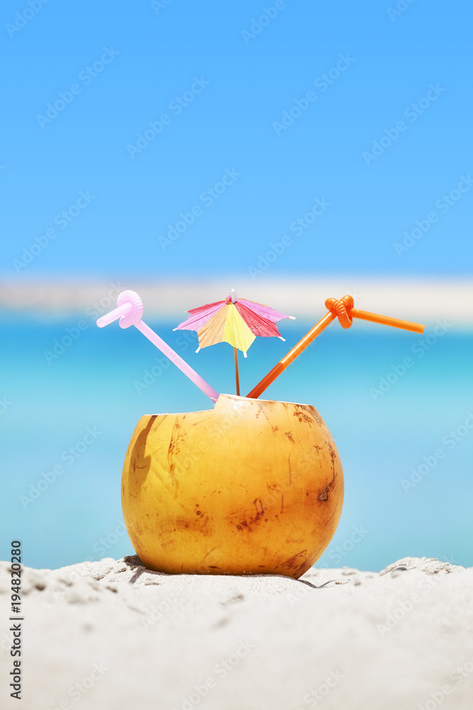 Close up picture of a coconut with two straws and colorful umbrella on a beach, summer holiday concept, selective focus. Close up picture of a coconut with two straws and colorful umbrella on a beach, summer holiday concept, selective focus.