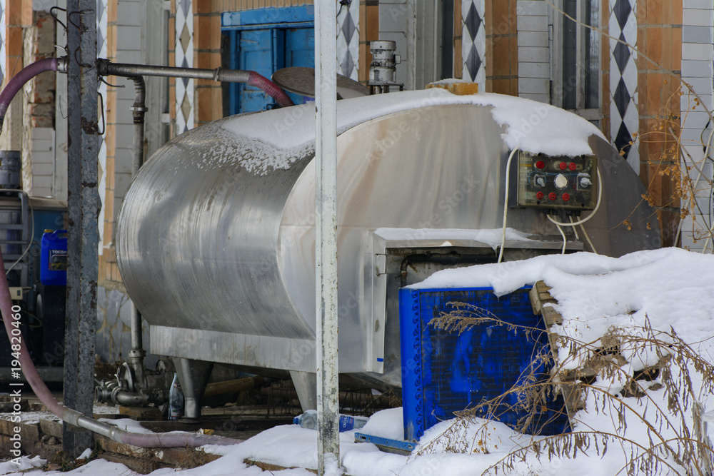 A large old tank for collecting milk in an abandoned and destroyed factory against a background of white snow in winter. Destruction and vandalism. Ukraine. A large old tank for collecting milk in an abandoned and destroyed factory against a background of white snow in winter. Destruction and vandalism. Ukraine.