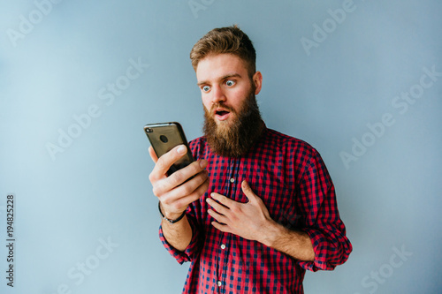 Hipster beard caucasian man with different surprising emotions holding smart phone on blue background.