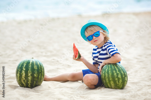 Adorable kid at the sea shore eating juicy watermelon. Cheerful child on summer time on the beach. Cute little boy outdoors photo