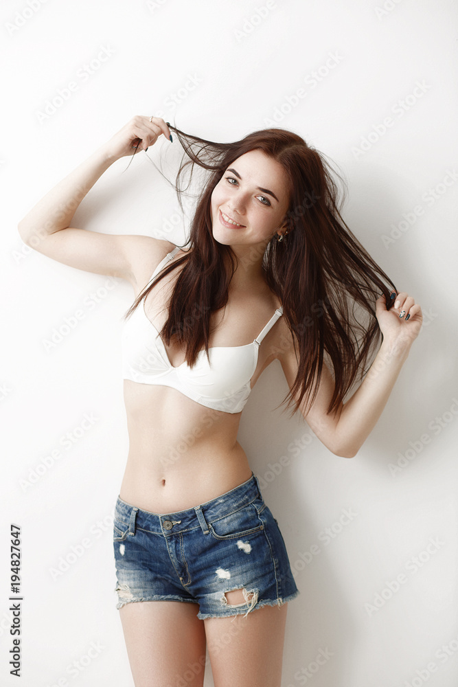 emotional portrait of a young, sexy girl in shorts and a bra on a white  wall background Stock Photo | Adobe Stock