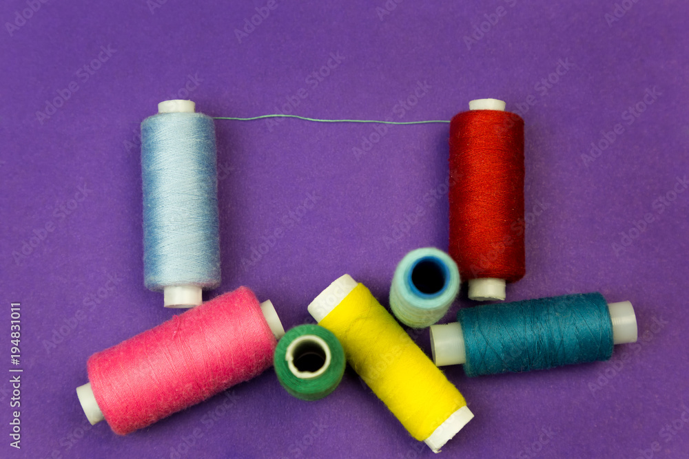 Several reels with threads on a blue background. The thread is stretched between the multi-colored thread coils. Several reels with threads on a blue background. The thread is stretched between the multi-colored thread coils.