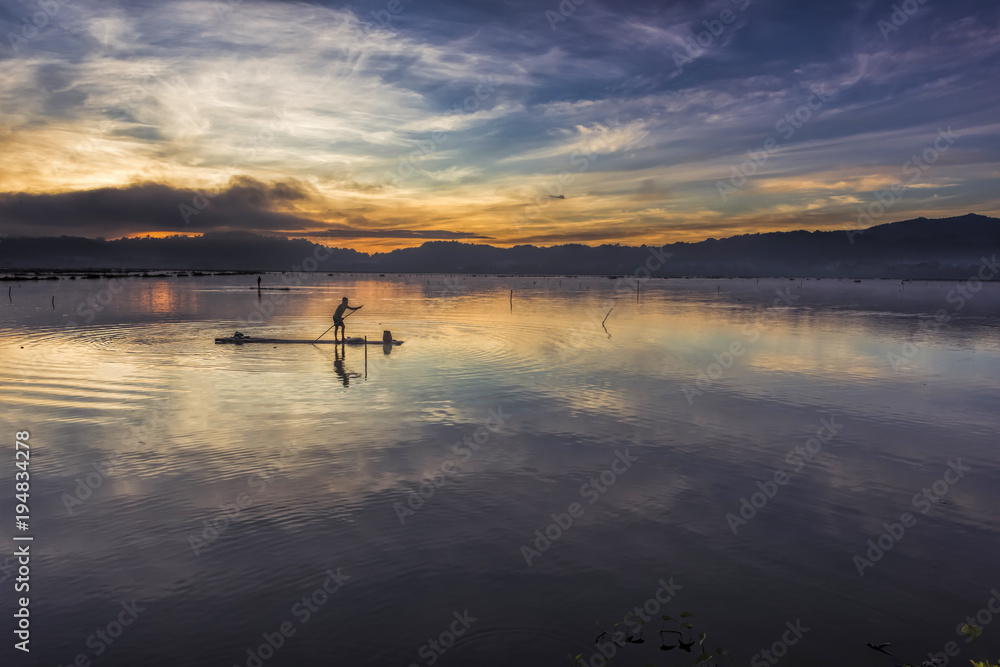 Fisherman silhouette with bamboo raft in water lake