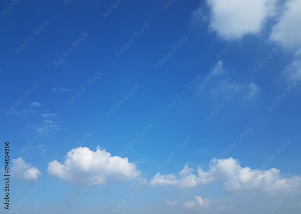 Clear sky with white puffy clouds and shades and hues of different blue with copy space