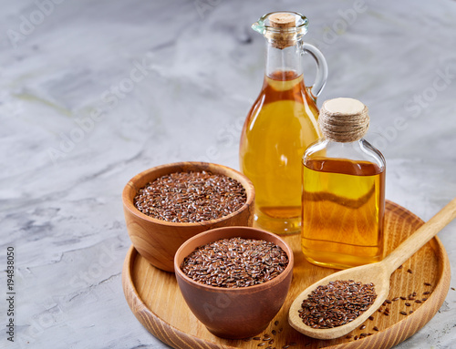 Flax seeds in bowl and flaxseed oil in glass bottle on light textured background, top view, close-up, selective focus