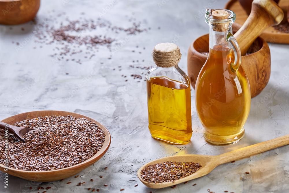 Flax seeds in bowl and flaxseed oil in glass bottle on light textured background, top view, close-up, selective focus Flax seeds in bowl and flaxseed oil in glass bottle on light textured background, top view, close-up, selective focus