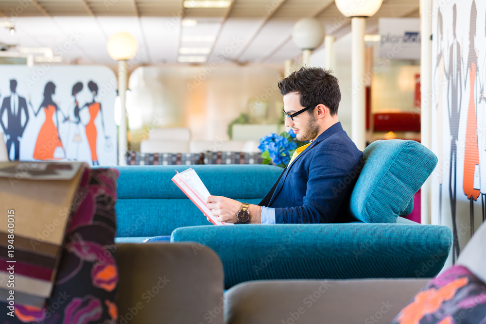 Young man reading hand-out and testing sofa in furniture store Young man reading hand-out and testing sofa in furniture store
