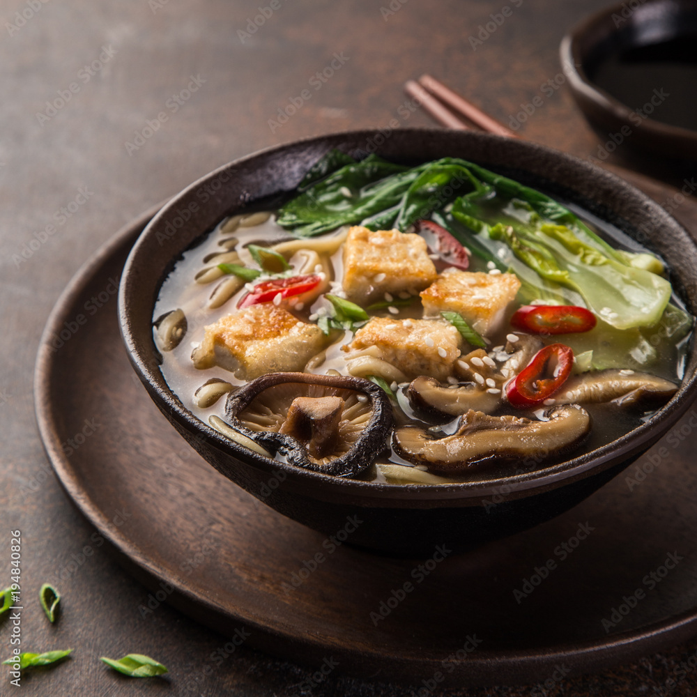 asian vegan noodle soup with tofu cheese, shiitake mushroms and pak choi, dark background