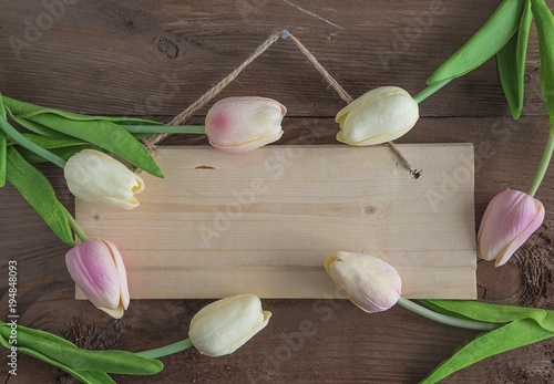 Wooden board decorated by pink and white tulips pending on dark wooden background