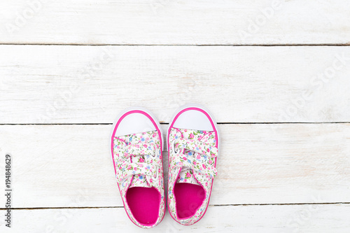 Pink sneakers for little girl on white wooden background. Flat lay