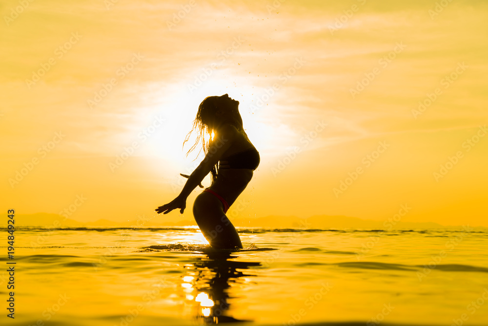 Silhouette of young girl in the water that splashing their hair against sunset