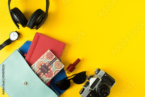 Flat lay of cute woman bag open out with passport, old camera, sunglasses, notebook, accessories and nail polish on colorful background with copy space, top view. All you need to comfort travel.