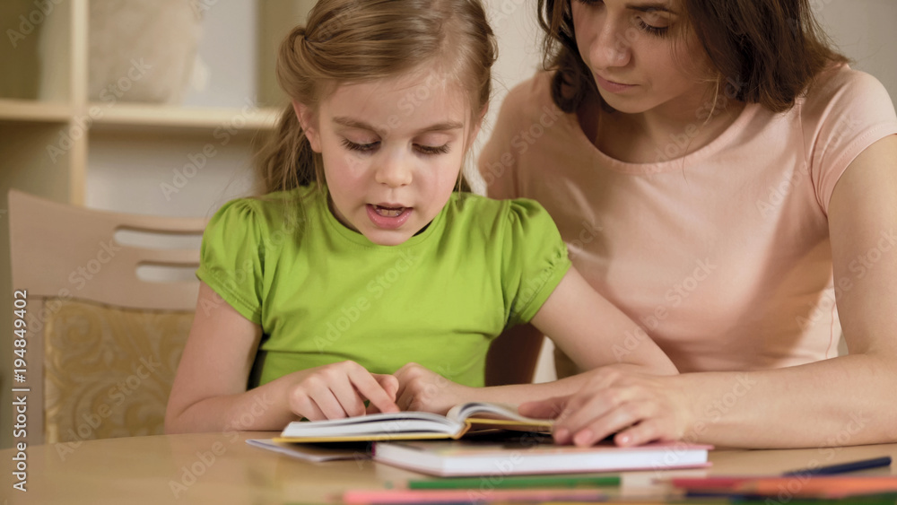 Girl reading interesting storybook for mother, woman proud of smart daughter Girl reading interesting storybook for mother, woman proud of smart daughter