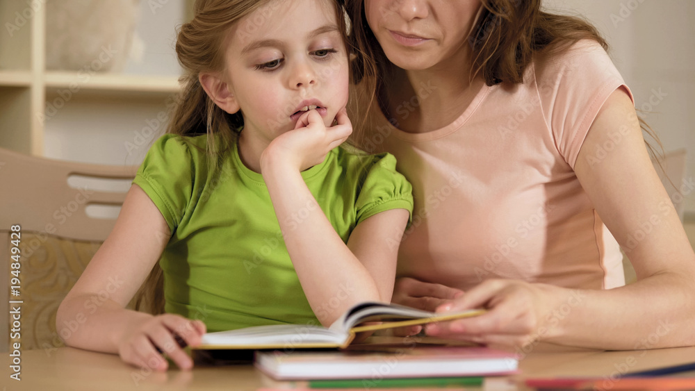 Supportive mother reading textbook together with hyperactive little daughter Supportive mother reading textbook together with hyperactive little daughter