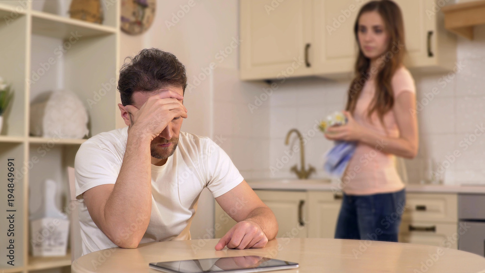 Fototapeta premium Wife scolding her unemployed husband at kitchen, chastising him for burning time