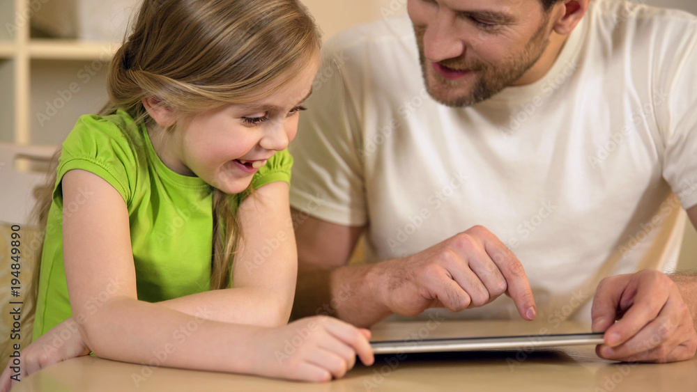 Happy father and daughter enjoying funny educational application on tablet pc Happy father and daughter enjoying funny educational application on tablet pc