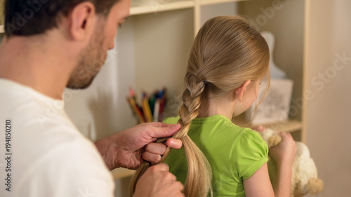Responsible good father braiding little daughters hair, preparations for school