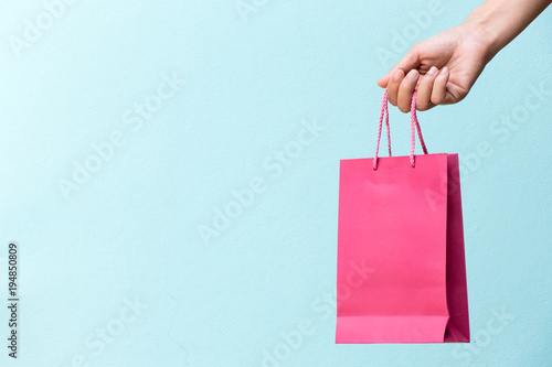 Hand of business woman hold pink shopping bag on blue concrete background