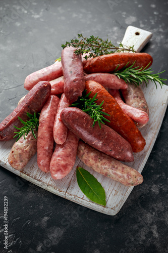 Freshly made raw breed butchers sausages mix in skins with herbs on white cutting board.
