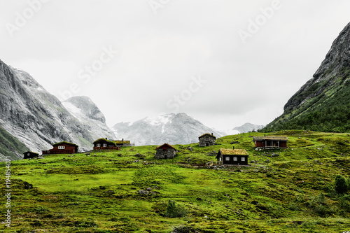 Beautiful grass roof cabins and houses in a green pastured valley surrounded by snow capped mountains in the winter in Western Norway