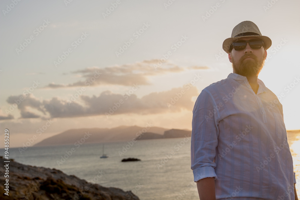 Red-bearded man of European appearance in the golden rays of the sun is at dawn against the backdrop of the sea and islands Red-bearded man of European appearance in the golden rays of the sun is at dawn against the backdrop of the sea and islands