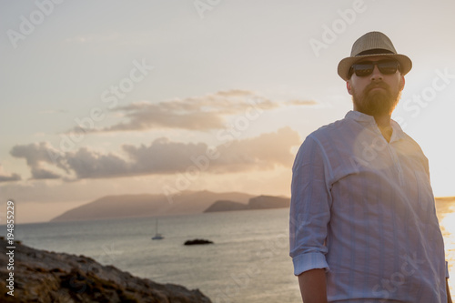 Red-bearded man of European appearance in the golden rays of the sun is at dawn against the backdrop of the sea and islands