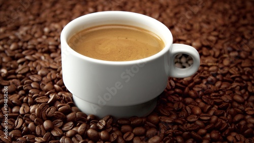 side view of white cup of black coffe on coffee beans. Coffee cream moving in cup © Anastasia