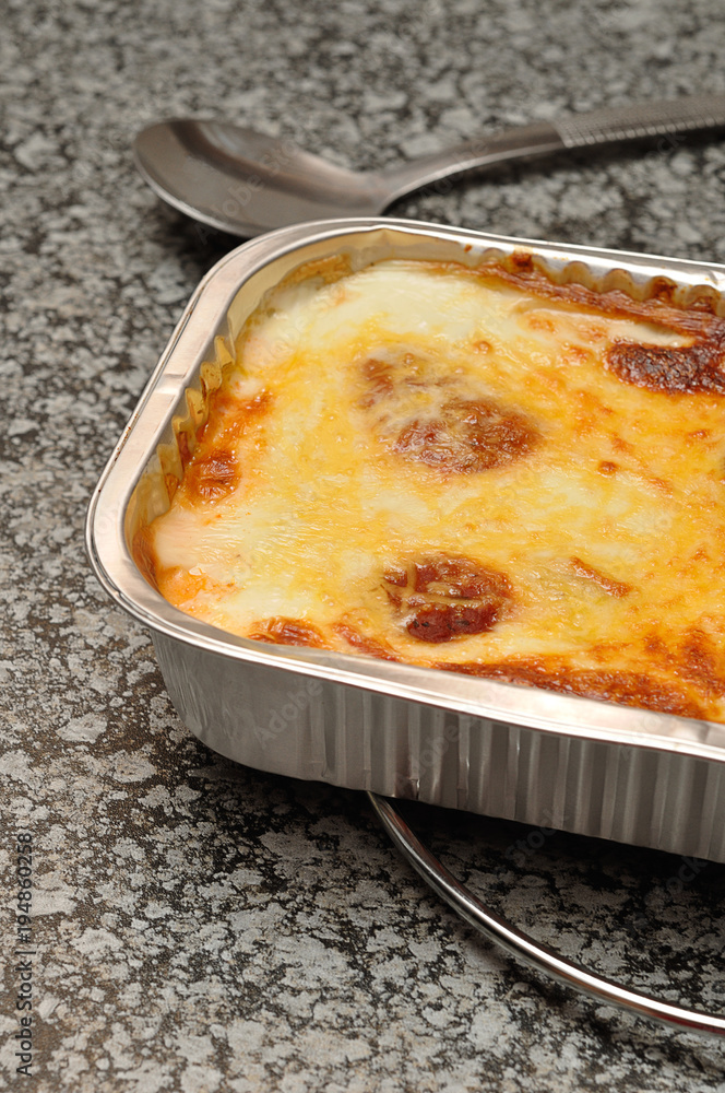 A golden brown lasagne displayed in a foil bake on a kitchen top A golden brown lasagne displayed in a foil bake on a kitchen top