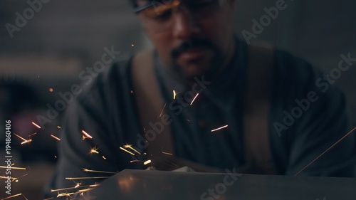Worker using industrial grinder. Worker in garage makes work with metall and grinder. flying sparks worker in blur, sparks in focus