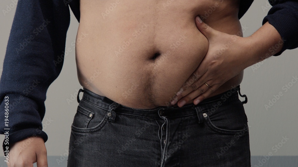 Naklejka premium overweight man closeup of belly front view. put up shirt and pinch and clap a belly
