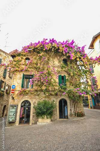 SIRMIONE, ITALY  Facade of house in center of Sirmione with flowering pink bougainvillea.traditional summer facade decoration of an old house in Italy, italy street.Old house covered by ivy
