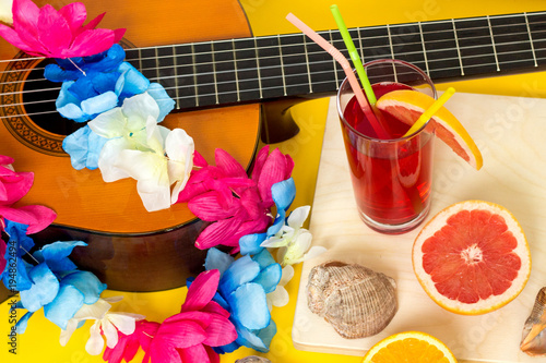 Hawaiian party concept: handmade DIY lei from faux flowers, alcohol-free fresh red drink and juicy fruits - orange and grapefruit, sea shells, vacation concept, flat lay on yellow background photo