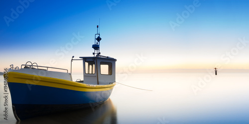 The rising sun illuminates the fishing boat. Baltic sea. Long exposure