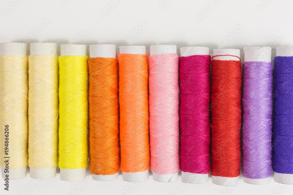 spools and bobbins of sewing thread in yellow, orange, pink, red and lilac spools and bobbins of sewing thread in yellow, orange, pink, red and lilac