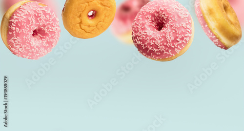Photography Falling or flying pink glazed doughnuts with sprinkles in motion at pastel blue