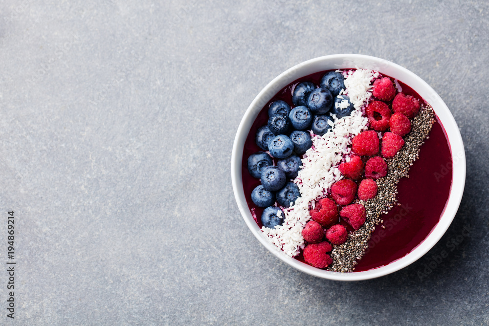 Smoothie bowl with fresh raspberry, blueberry, coconut flakes and chia seeds. Grey stone background. Top view. Copy space. Smoothie bowl with fresh raspberry, blueberry, coconut flakes and chia seeds. Grey stone background. Top view. Copy space.