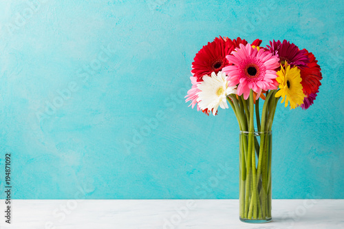 Fototapeta Naklejka Na Ścianę i Meble -  Colorful bunch of gerbera flowers in a glass vase. Blue background. Copy space.