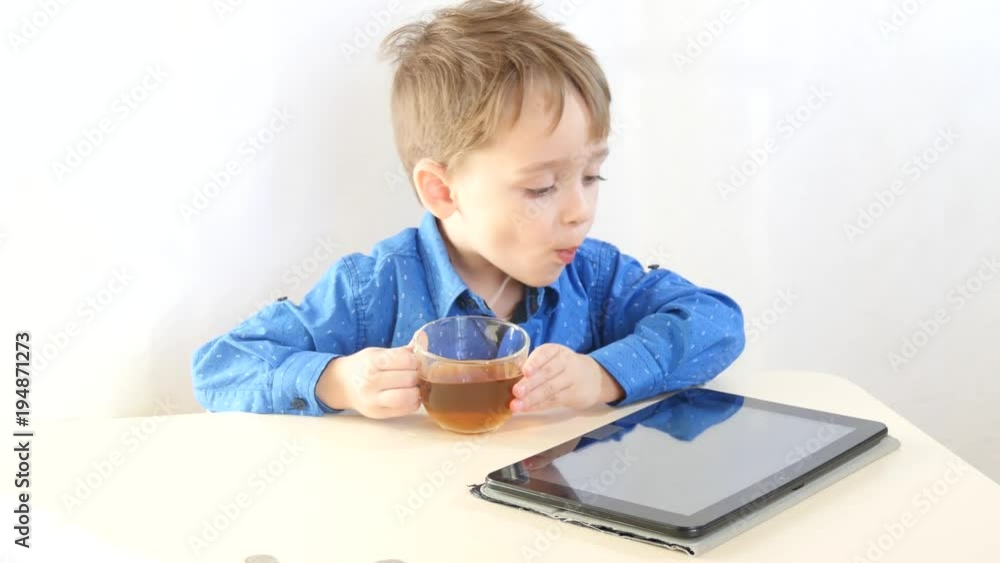 A child is playing with a tablet, in breaks, drinking tea. Internet and wireless technologies. The concept of child development. A child is playing with a tablet, in breaks, drinking tea. Internet and wireless technologies. The concept of child development.