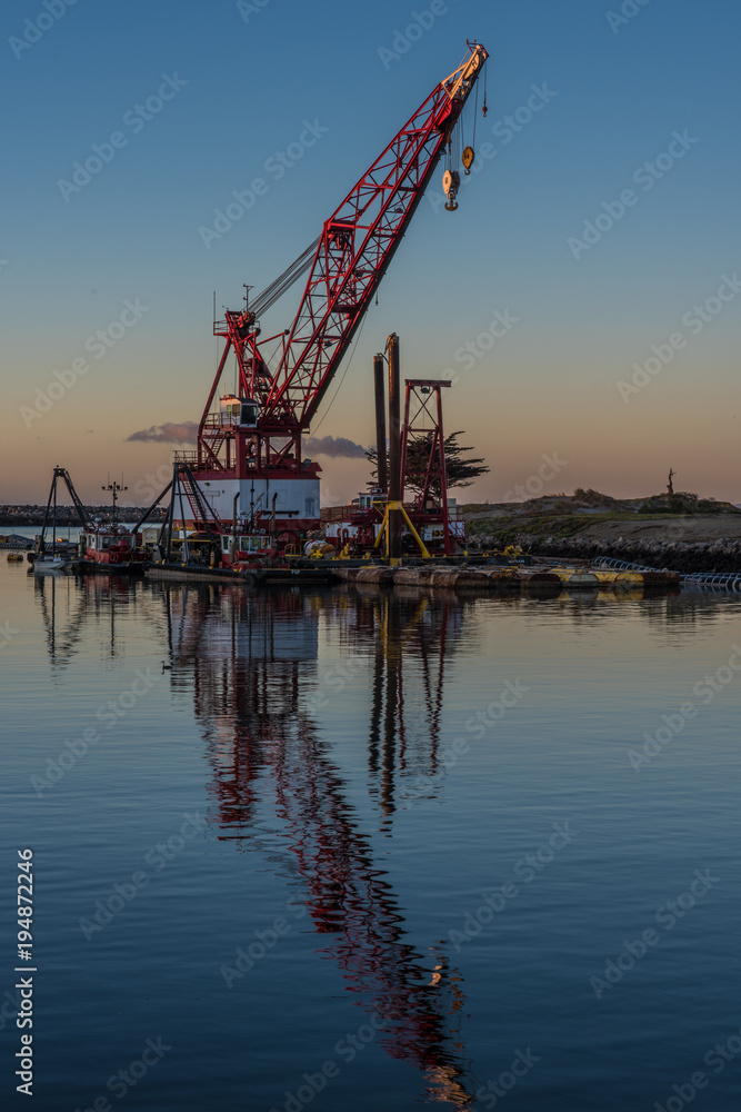 Marine floating crane reflected in calm water of the cove in the early hours of dawn.