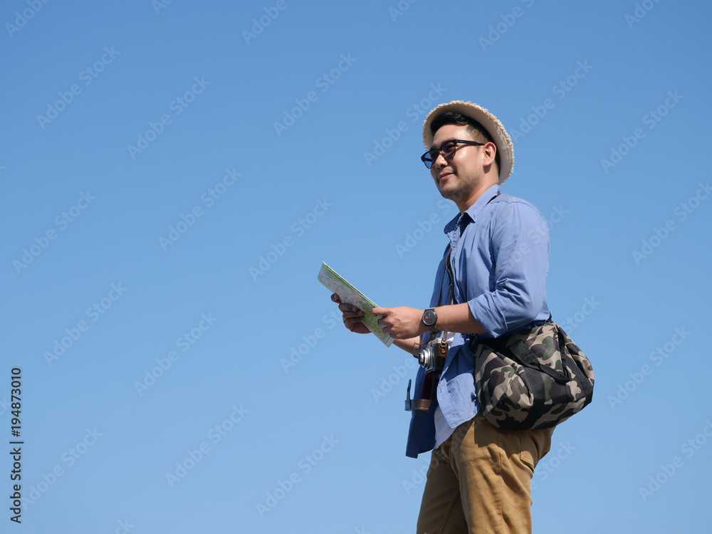 Naklejka premium Asian man travel with map and vintage camera on blue sky background