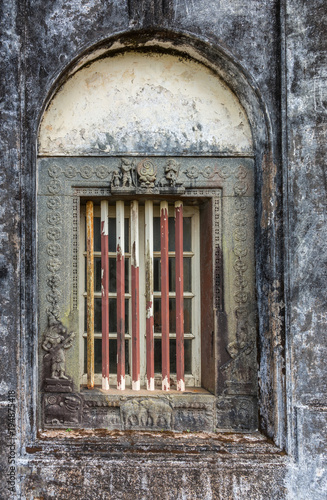 Madikeri  India - October 31  2013  Closeup of window and rusty decorated metal frame of Royal mausoleum  set in white wall devastated by black mold. Hindu figurines.
