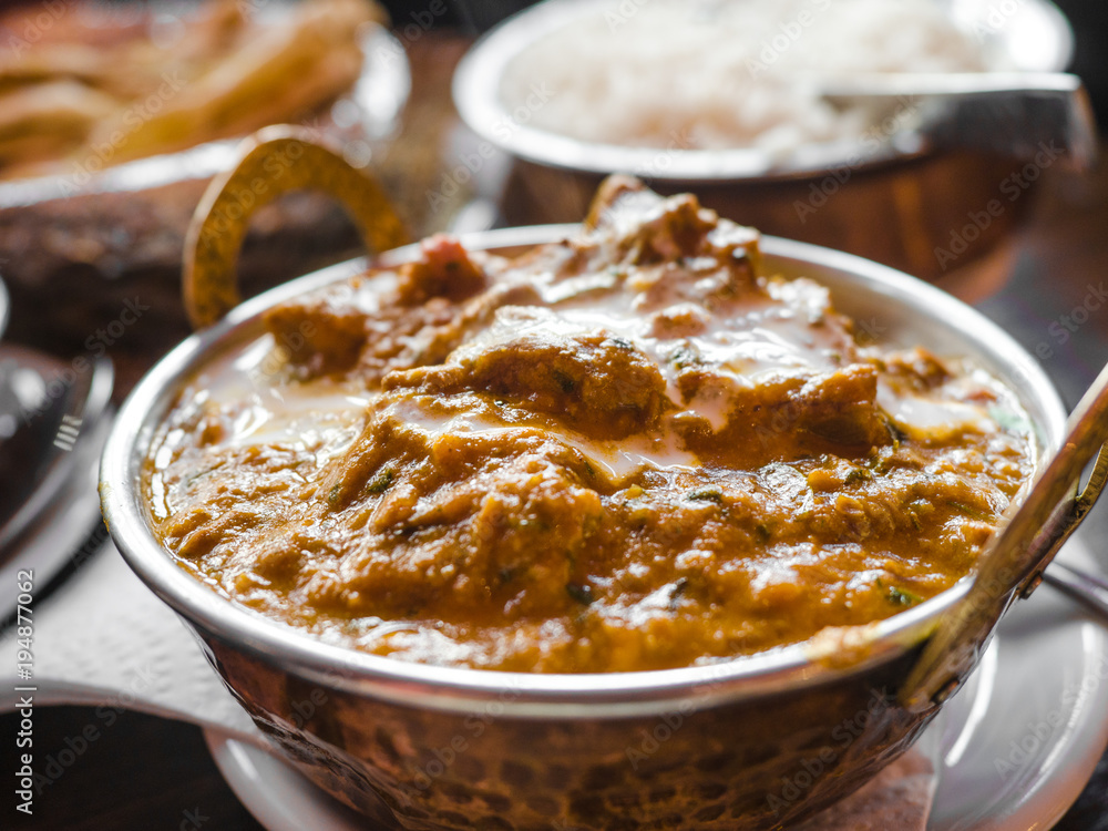 Indian Food or Indian Curry in a copper brass serving oriental bowl, pieces of chicken fillet in curry sauce ingredients in a pan with the old table side view close-up, Set of Indian food. Indian Food or Indian Curry in a copper brass serving oriental bowl, pieces of chicken fillet in curry sauce ingredients in a pan with the old table side view close-up, Set of Indian food.