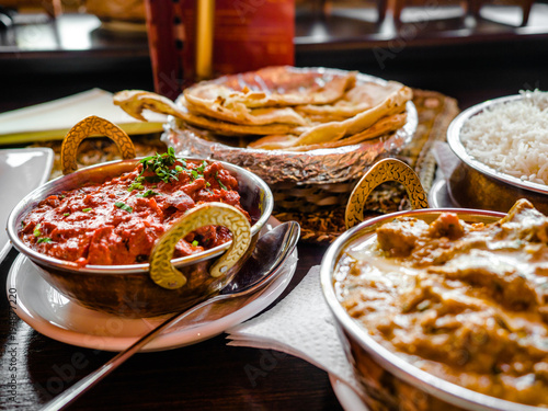 Indian Food or Indian Curry in a copper brass serving oriental bowl, pieces of chicken fillet in curry sauce ingredients in a pan with the old table side view close-up, Set of Indian food.