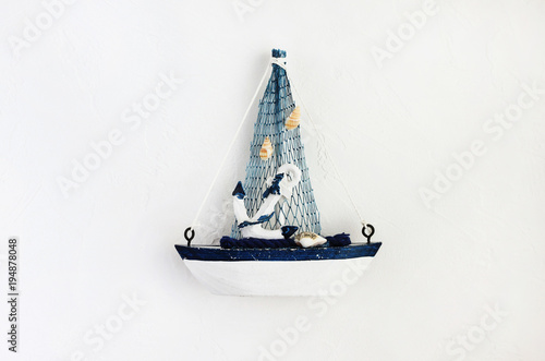 Small toy boat on white concrete background top view, white and blue simple colors. Inspirational marine traveling decor. 