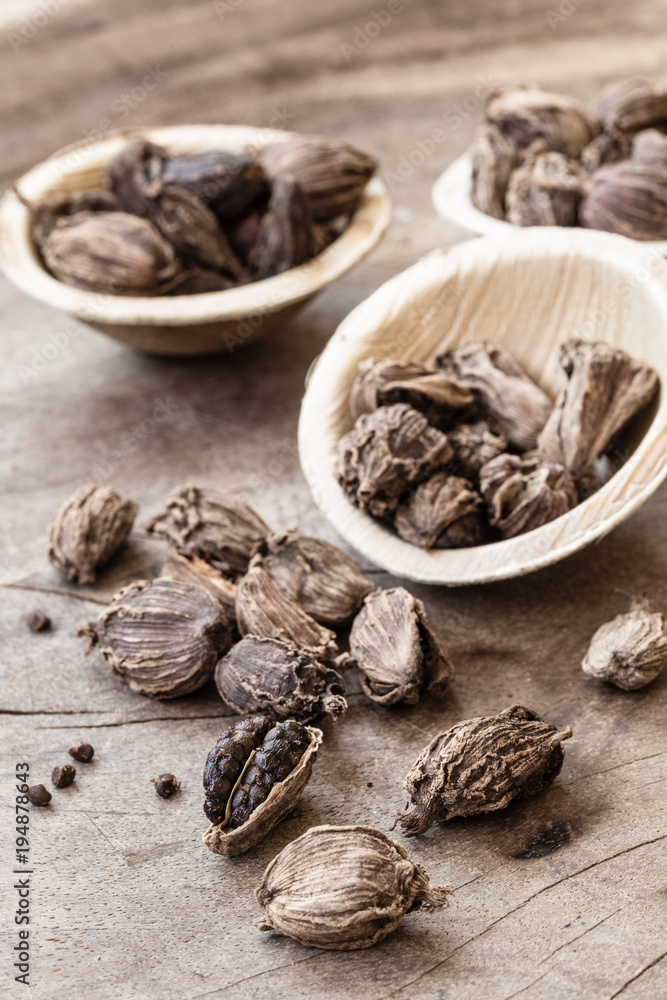 Black cardamom whole seed in a bowl on wooden background Black cardamom whole seed in a bowl on wooden background